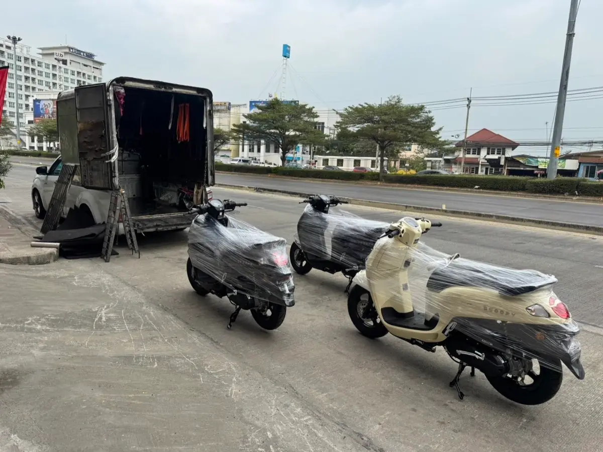 Three film-wrapped scooters lined up by the box truck